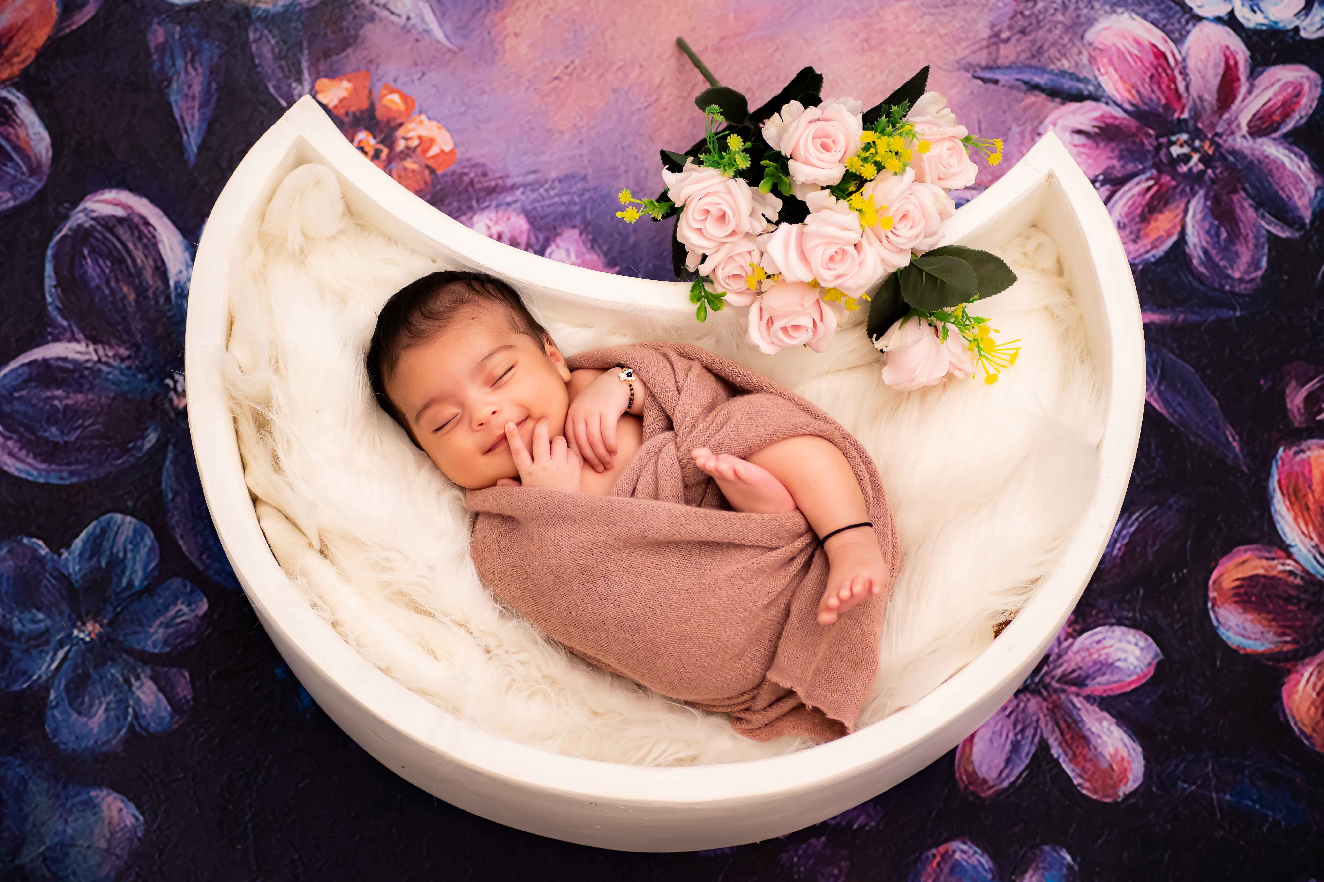 A precious newborn baby resting in a tiny moon-shaped tub, wrapped in a brown sheet, captured during a peaceful baby photoshoot.
